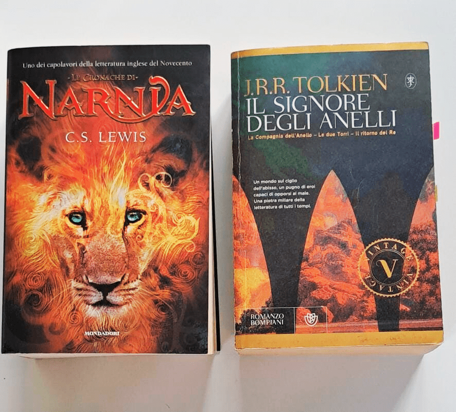 Copertina italiana dei romanzi "Le Cronache di Narnia" di C.S. Lewis e "Il Signore degli Anelli" di J.R.R. Tolkien, edizioni Mondadori e Bompiani, fotografati affiancati su un tavolo bianco.
